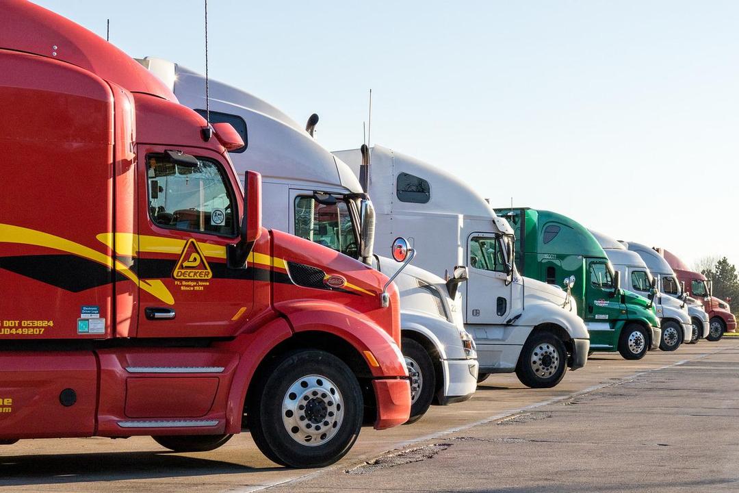 A row of semi-trucks parked in a lot. The trucks are various colors, including red, white, and green.